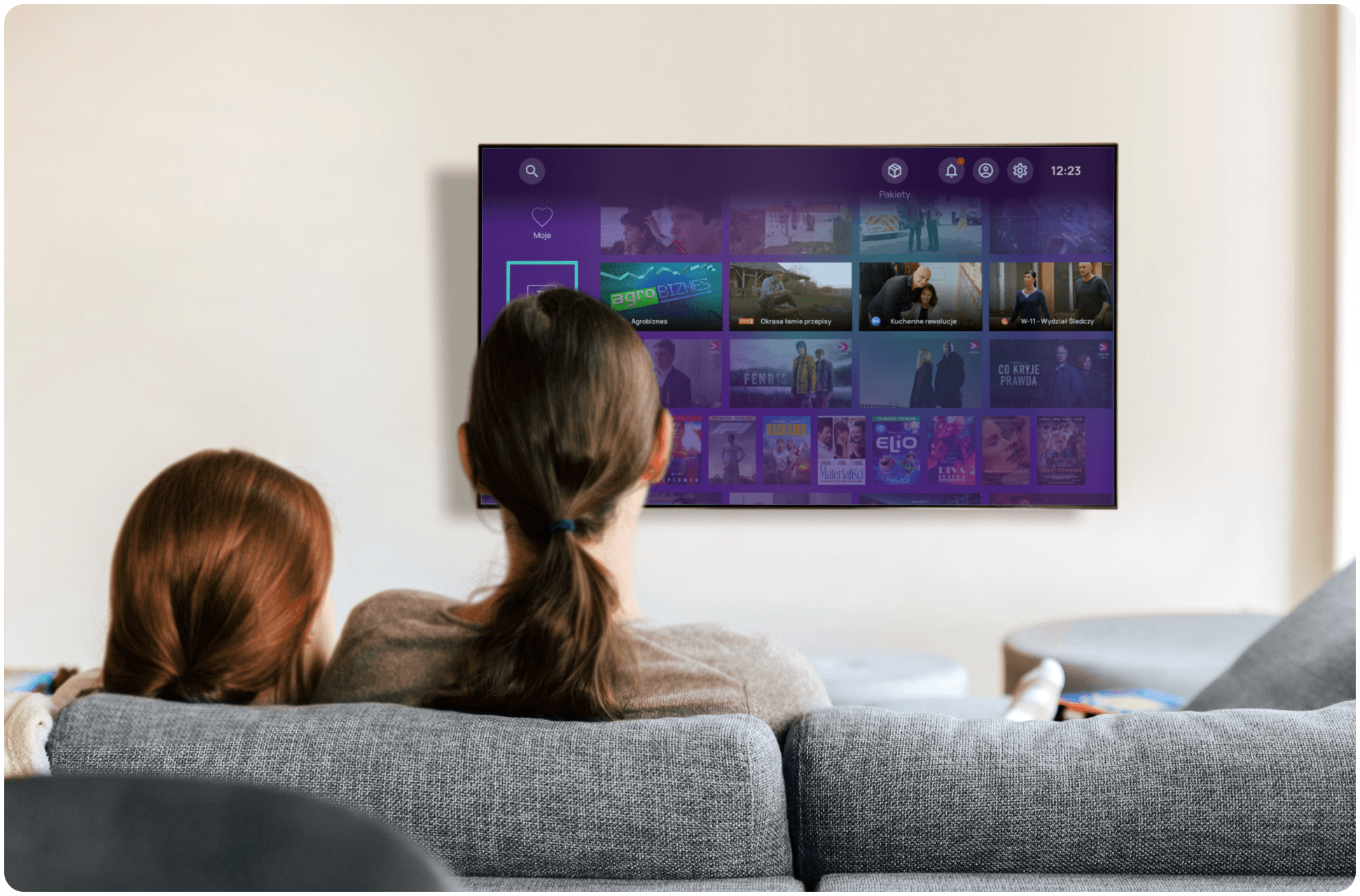 Two people on a sofa watching a TV platform home screen with a catalogue of films and series